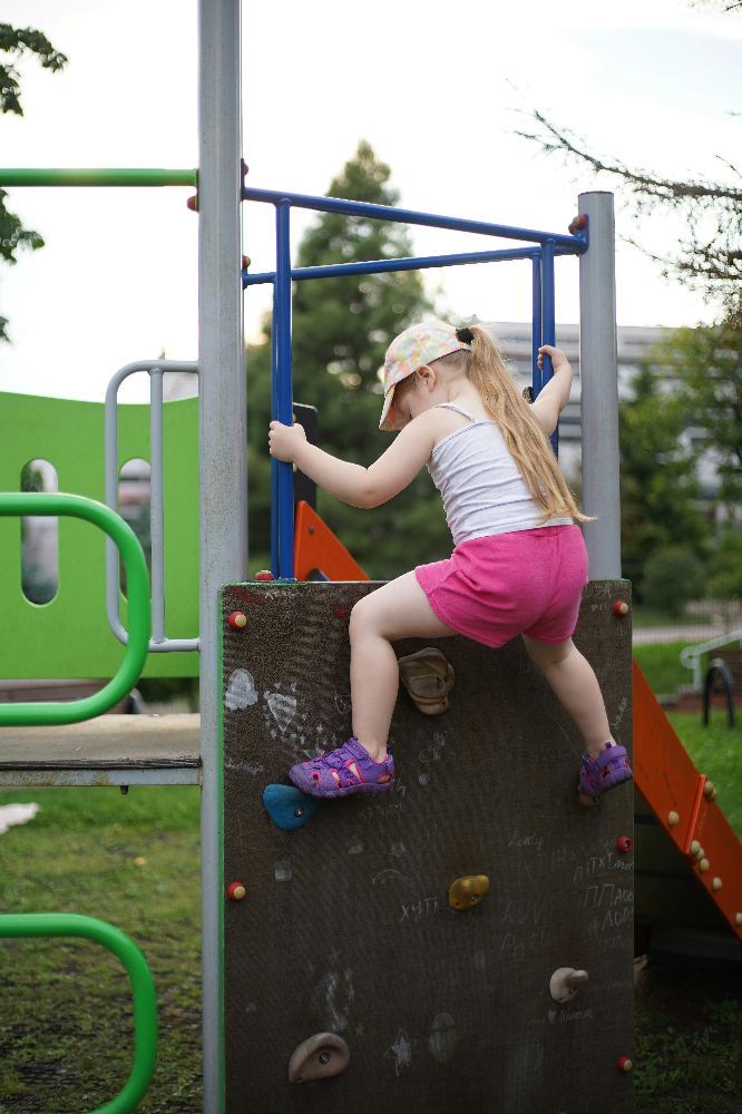 Child climbing commercial playground equipment with protective playground safety surfacing designed to reduce injuries from falls in public play areas